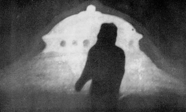 Vénusien qui a permis à Howard Menger de prendre en photo sa silhouette en face du vaisseau illuminé. Les visiteurs de l’espace ne désirent pas des photographies claires d’eux-mêmes car ils pourraient être reconnus ensuite sur Terre (ils sont en infiltration partout). Une aura de champ de force peut être vue autour du vaisseau spatial dans la photo originale, qui assez visible sur cette reproduction imprimée.