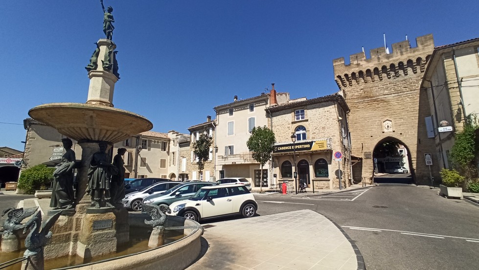 L'horloge électrique sur la porte médiévale est en face de la place avec la fontaine, lieu d'où part Pierre Monnet, prise en photo à Courthézon par le rédacteur de cet article au début du mois d'août 2025.