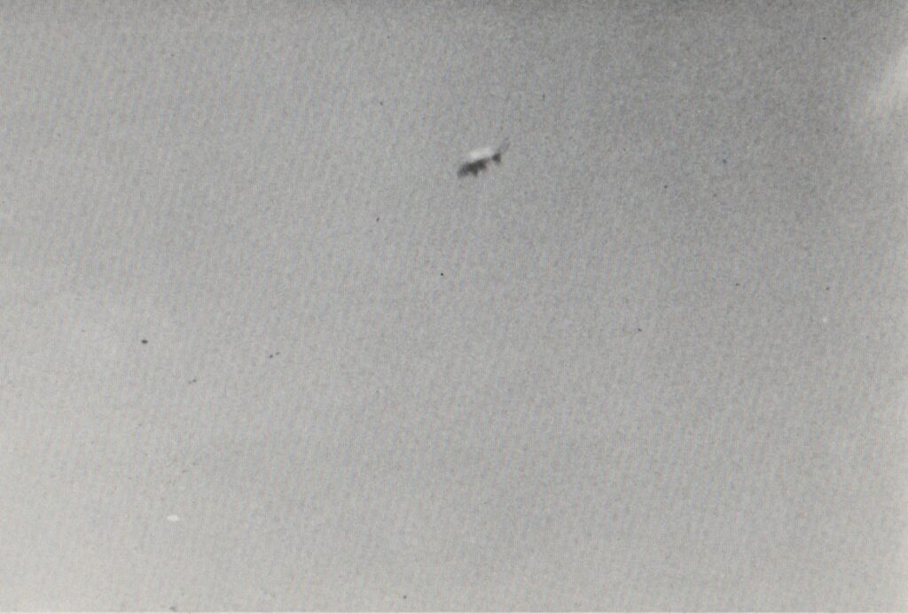 22 janvier 1978, de 10h20 à 11h05, Dorchester Road à Forest Hills. La photo numéro 8 montre un objet argenté surmonté d’un dôme blanc, avec une collerette rouge orangé autour du rebord et des protubérances sous la surface inférieure du vaisseau incliné vers la gauche.