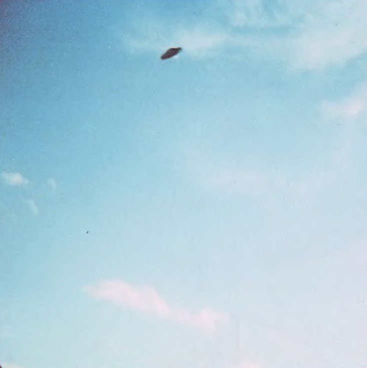 4 avril 1980. Cette douzième et dernière prise de la série de photos a capturé le vaisseau de Zeta Reticuli alors qu’il commençait à s’élever avant de quitter la zone. Il est parti dans un arc diagonal rapide, hors de portée visuelle. Bien que le vaisseau semble apparaître à l’envers ici, cela est dû uniquement à l’angle du soleil couchant frappant le dessous de l’appareil, qui possédait également un dôme surélevé en métal similaire, apparemment de taille égale à celui du dessus.