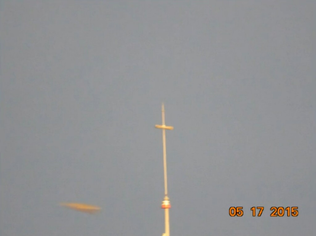 Photo d'un engin volant prise par José Yaguana depuis la terrasse de sa maison, avec zoom. On voit une antenne à droite et l l'engin volant en forme de losange qui circulait lentement dans le ciel à gauche. José l'a pris volontairement en photo car il l'observait dans le ciel, ce n'est pas un engin observé sur la photo au développement avec surprise, il était bien visible dans le ciel. José précise que les gens passaient dans la rue mais pas un seul ne levait les yeux vers le ciel pour voir l'appareil. Les gens qui passaient regardaient José qui photographiait le ciel et n'avaient même pas la curiosité de regarder en direction de ce que José photographiait.