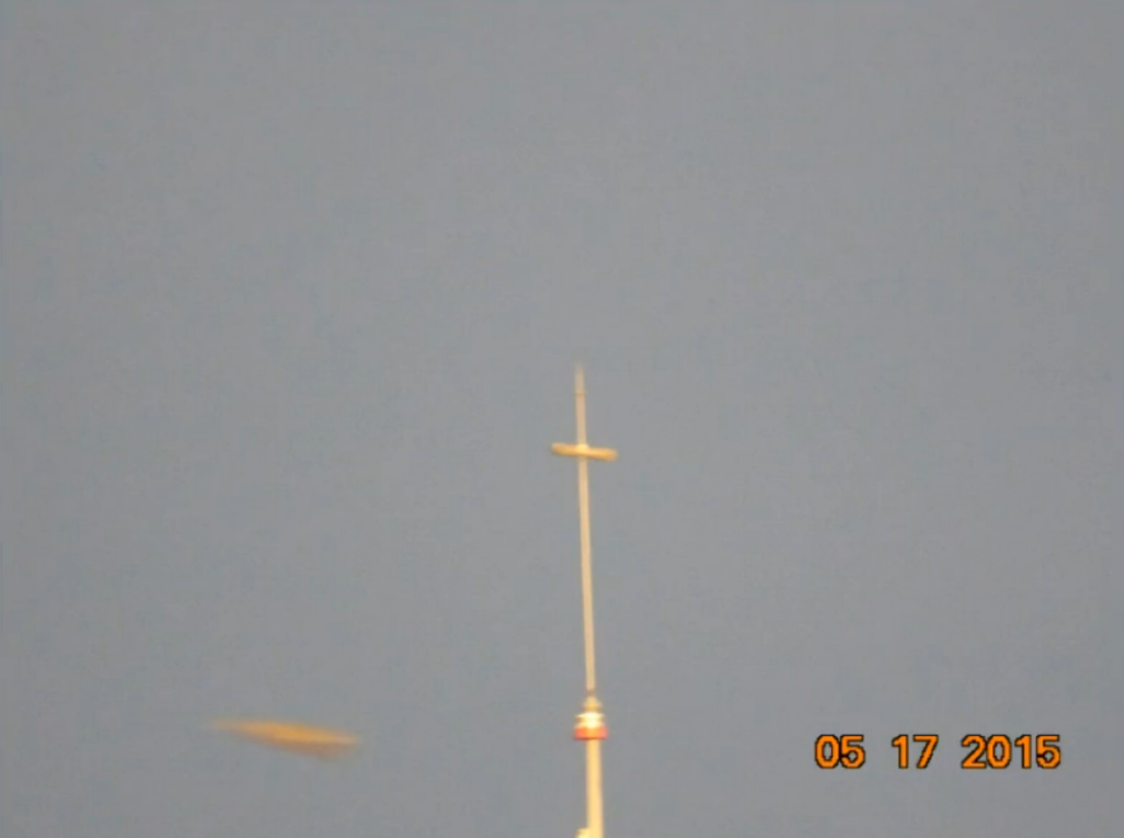 Photo d'un engin volant prise par José Yaguana depuis la terrasse de sa maison, avec zoom. On voit une antenne à droite et l l'engin volant en forme de losange qui circulait lentement dans le ciel à gauche. José l'a pris volontairement en photo car il l'observait dans le ciel, ce n'est pas un engin observé sur la photo au développement avec surprise, il était bien visible dans le ciel. José précise que les gens passaient dans la rue mais pas un seul ne levait les yeux vers le ciel pour voir l'appareil. Les gens qui passaient regardaient José qui photographiait le ciel et n'avaient même pas la curiosité de regarder en direction de ce que José photographiait.