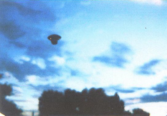 Ce dernier cliché montre la même silhouette en forme de tee de golf ressemblant à un vaisseau de Nep-4, se détachant sur un ciel bleu chargé de nuages, au-dessus des arbres. L’une des petites protubérances orange situées sous l’appareil semble cette fois produire une lueur. Les objets photographiés au cours des deux observations paraissent identiques par leur forme générale, mais aucune identification certaine de leur nature n’est donnée.